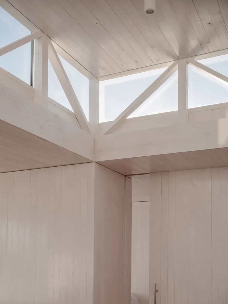 Upward view of the timber-framed clerestory window assembly with triangular bracing under a pale wood ceiling