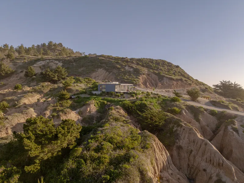 Long view of the house positioned on the eroded hillside ridge among scrub vegetation and exposed rock