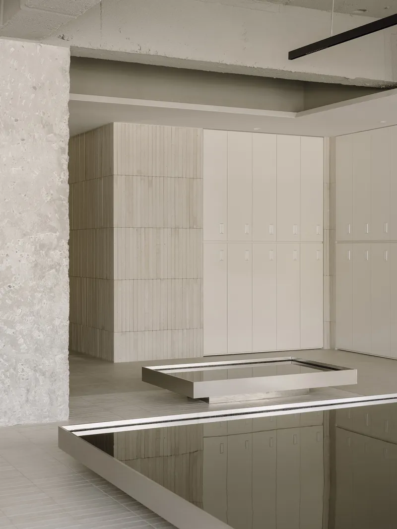 Pale timber locker wall next to concrete column with reflective pool edge in the foreground