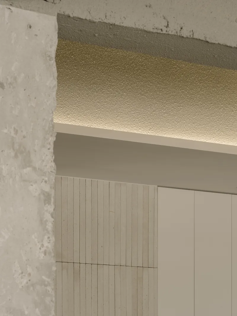 Detail of textured ceiling with concealed lighting adjacent to exposed concrete column and timber wall