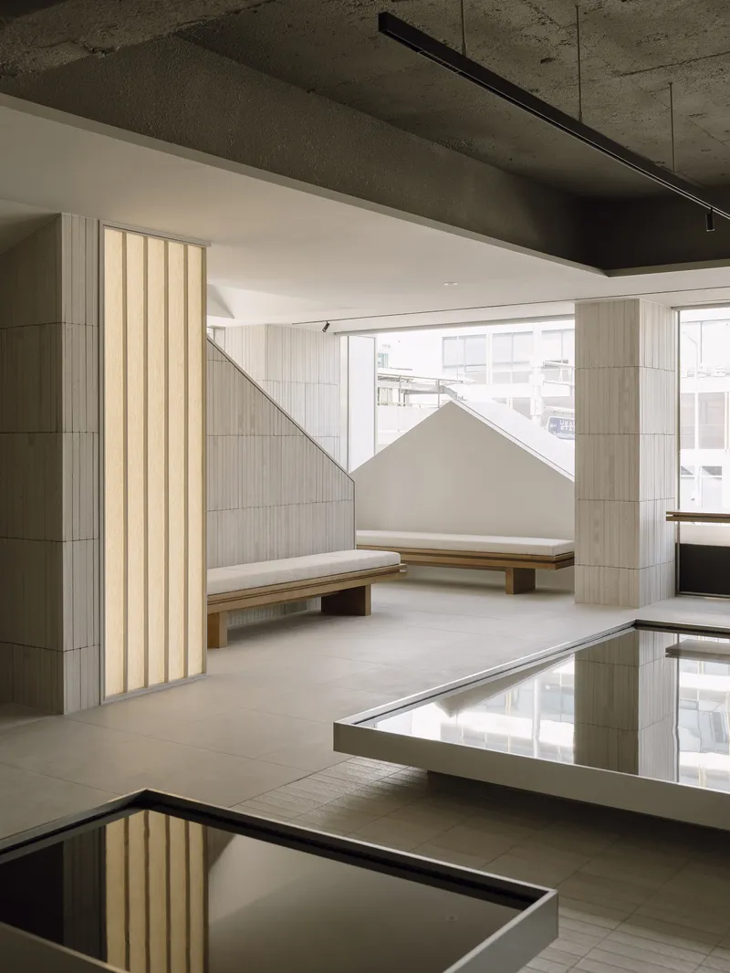 Seating niche with vertical fluted wall panel and timber benches beside mirrored floor inset