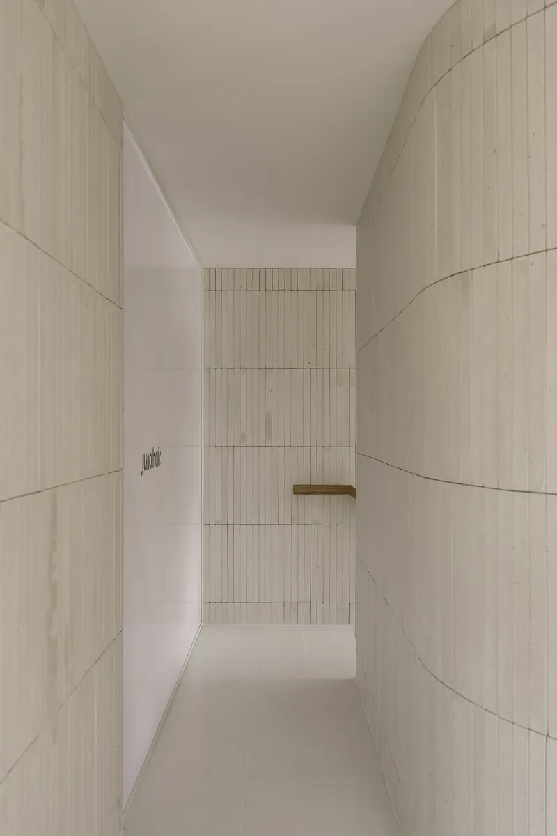 Narrow corridor flanked by curved ribbed tile walls leading to distant timber handrail
