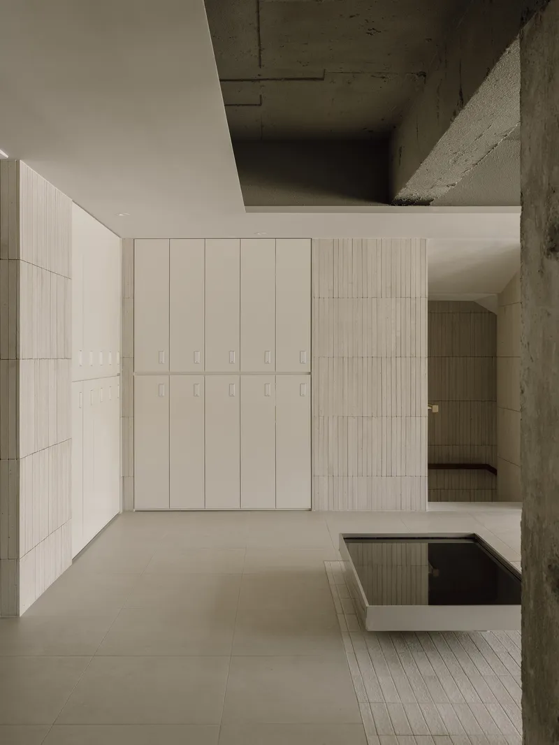 Interior view of pale tiled walls and exposed concrete ceiling framing a double-height salon space