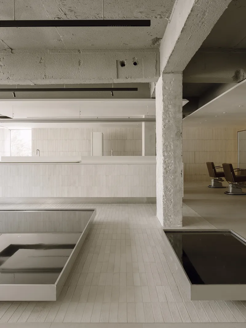 Concrete columns and exposed ceiling beams above linear salon counters clad in cream tile