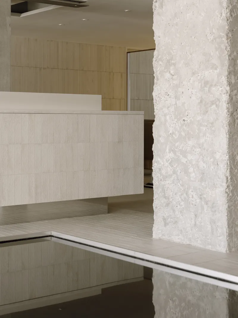 Close-up of textured white concrete column beside a pale tiled reception desk