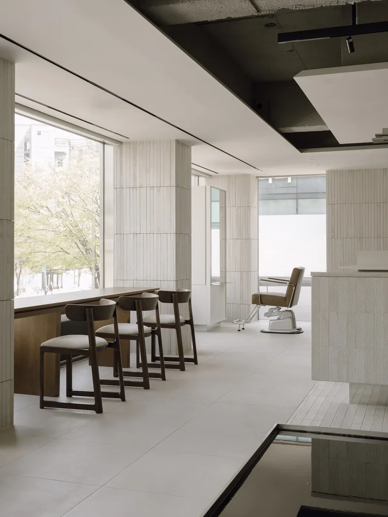 Row of wooden salon chairs facing floor-to-ceiling windows with spring trees visible outside