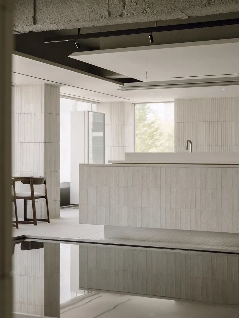 Salon workspace with light wood island and reflective dark water feature below exposed concrete beams