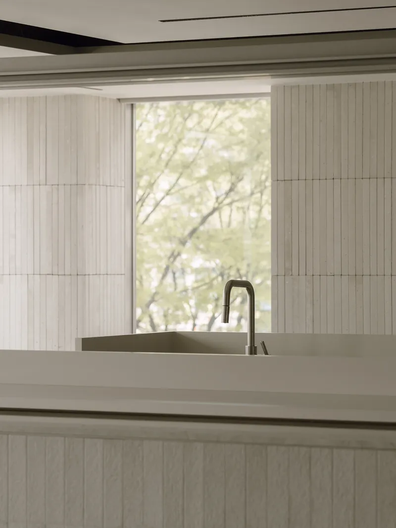 Kitchen island with integrated sink and tall faucet framed by vertical timber paneling and soft daylight