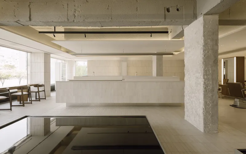 Reception desk with exposed concrete column and ceiling alongside a recessed floor pool reflecting overhead beams