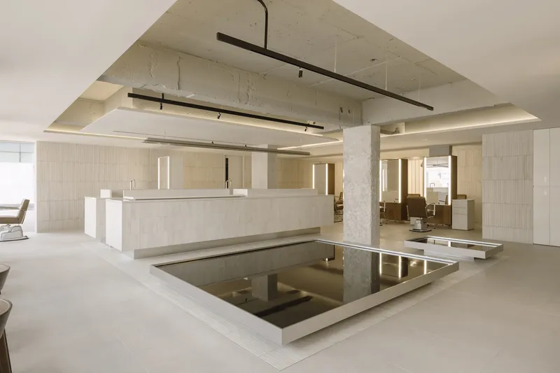 Central reception counter with suspended light fixtures and dark reflective pool set into pale flooring