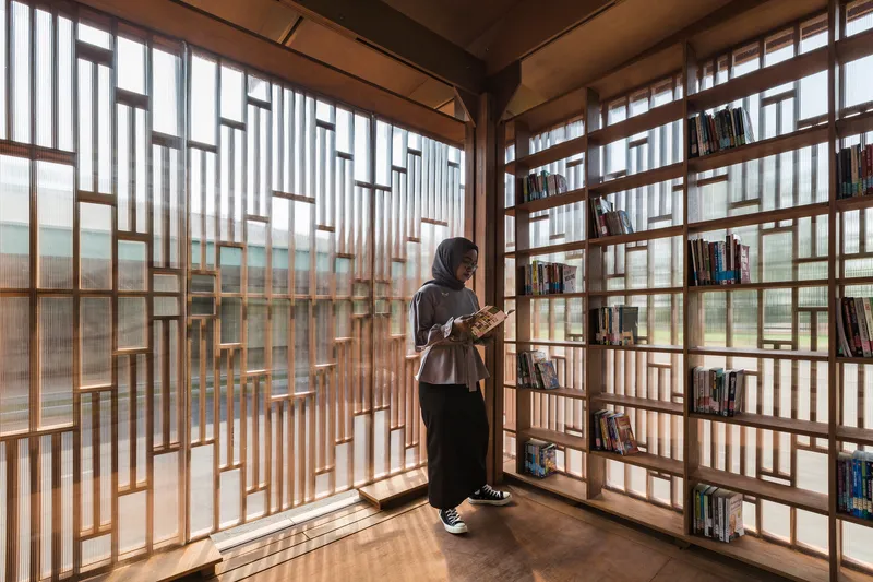 Interior library corner with geometric timber screen walls and shelving as a woman reads by the window