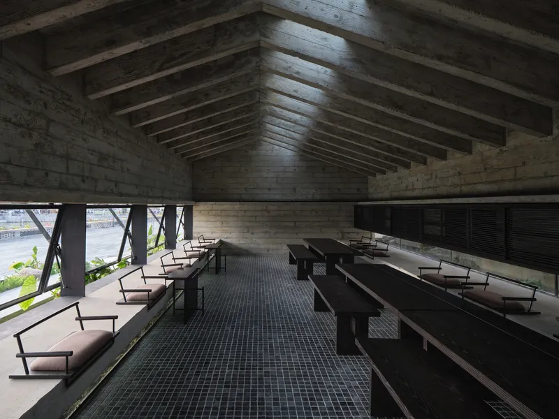 Interior hall with exposed timber ceiling beams, board-formed concrete walls and rows of benches