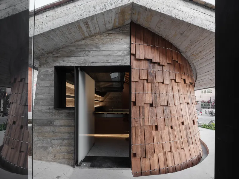 Curved timber-shingled wall wrapping a glazed entrance vestibule with concrete ceiling above