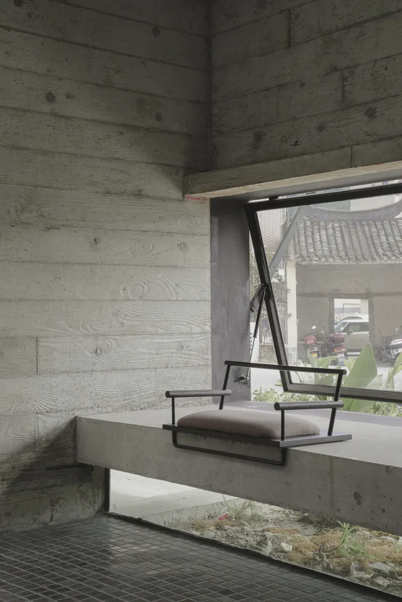 Concrete bench seat beneath board-formed walls and angled window framing planted courtyard beyond