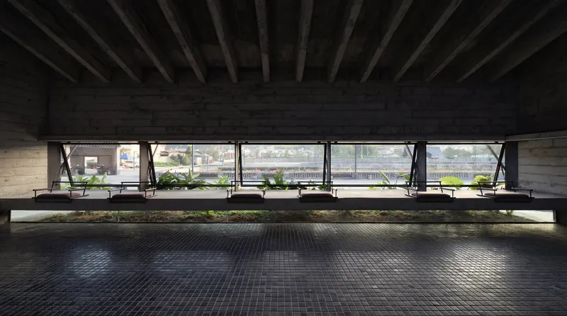 Covered plaza with exposed timber beams and planted beds along a continuous horizontal window band