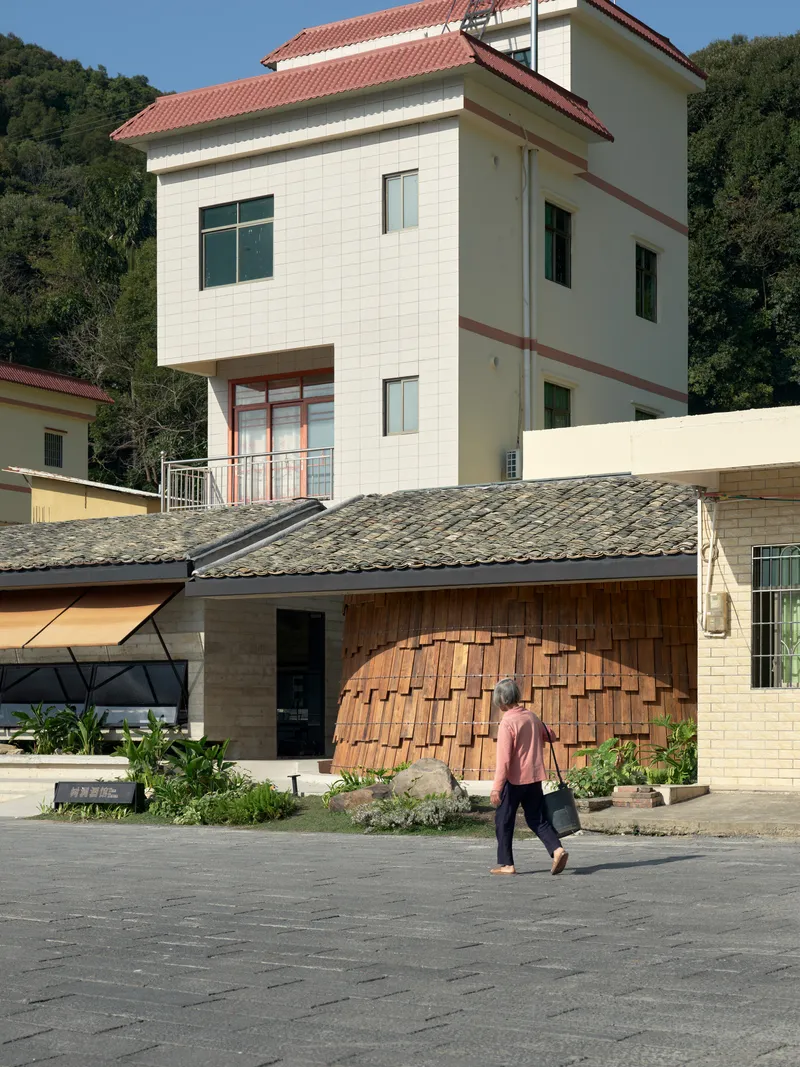 Arched timber screen facade with a person walking across the paved courtyard