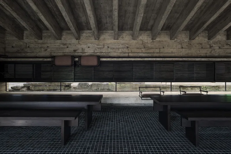 Interior hall with black steel benches under timber ceiling beams and horizontal window shutters