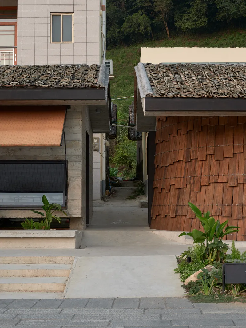 Concrete pathway between two volumes with ceramic tile roofs and green hillside beyond