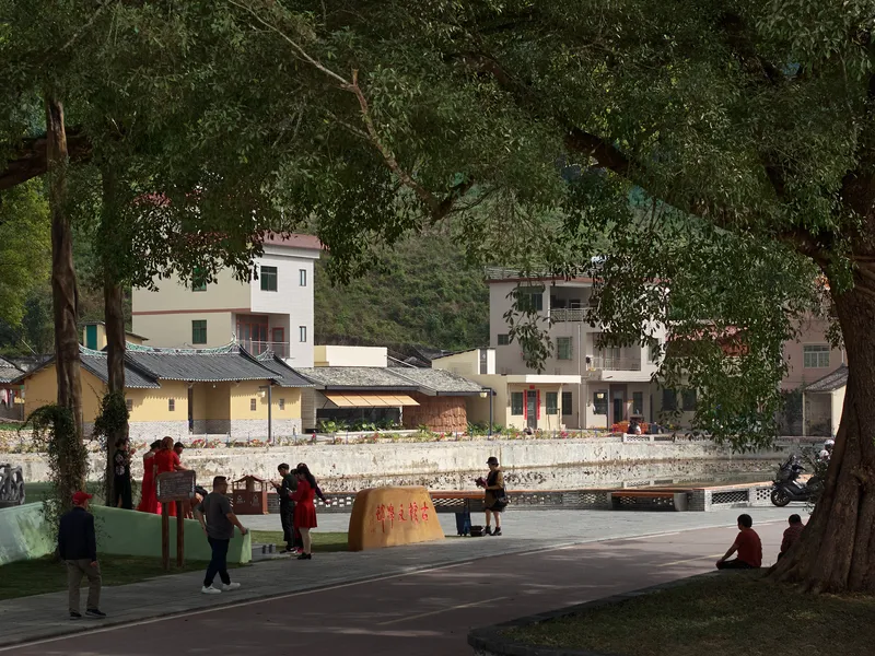 Low tiled roof pavilion viewed from plaza with visitors gathered beneath mature trees