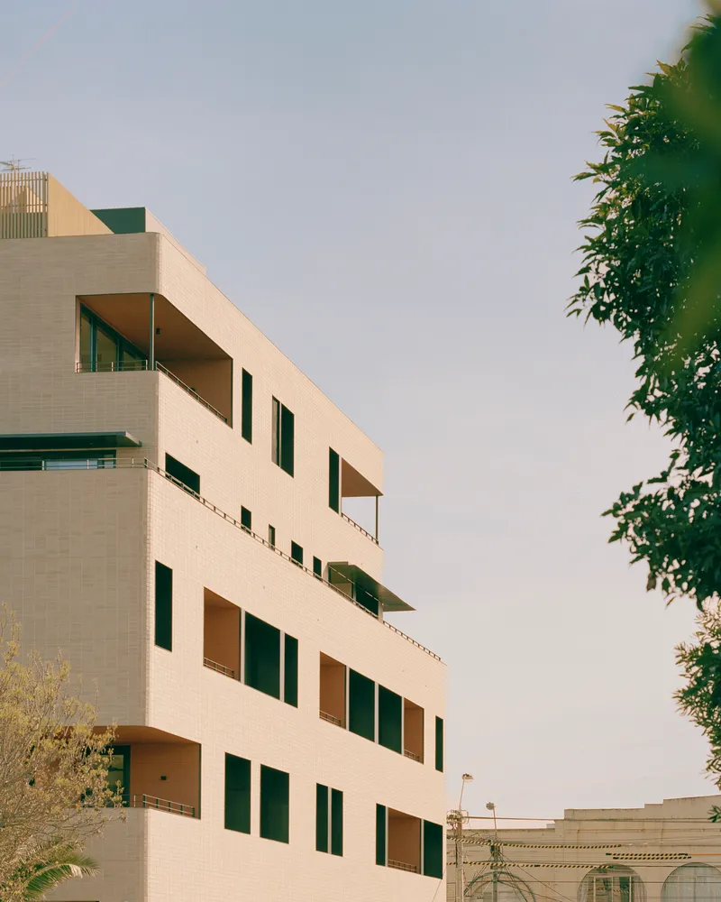 Upper floors of the cream tile facade with staggered terraces framed by foliage