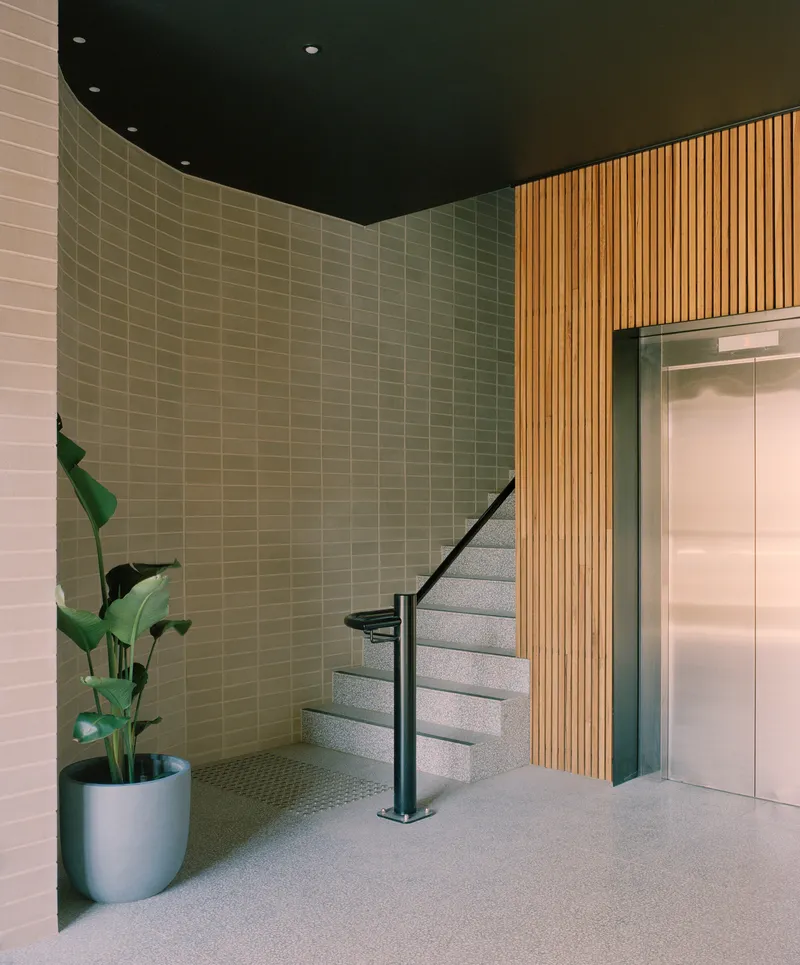 Ground floor lobby with terrazzo stair, vertical timber slats and potted plant
