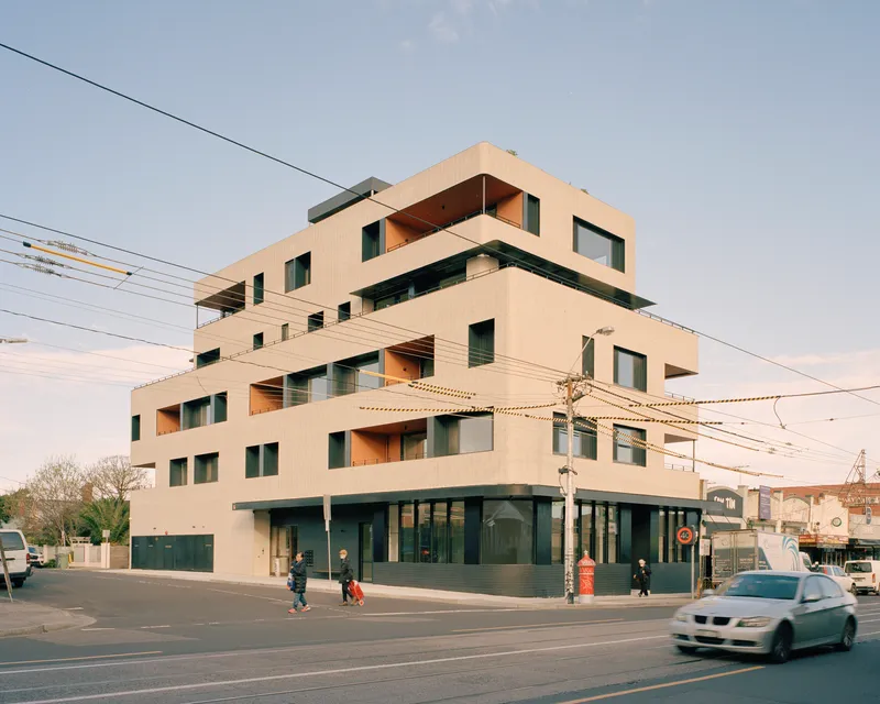Corner view of the stacked residential volume with pale tile cladding and pedestrians crossing below power lines