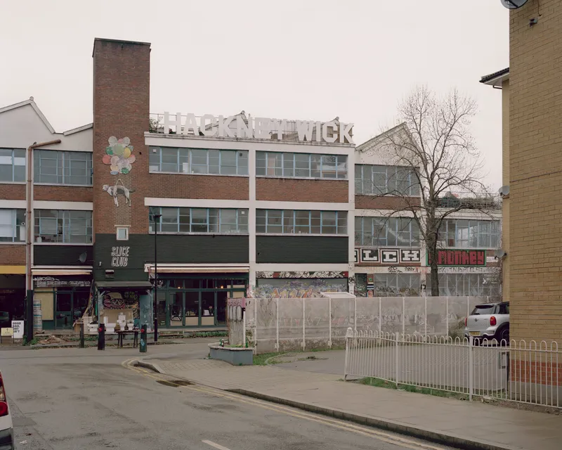 Street view of a mixed-use block with brick tower and horizontal bands of windows beneath an overcast sky