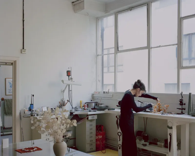 Workshop space with green work surface and an occupant leaning over the counter near tall metal-framed windows