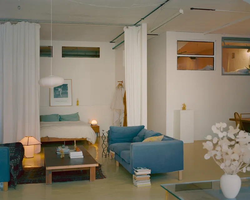 Open-plan living space with white curtain room dividers and clerestory windows at dusk