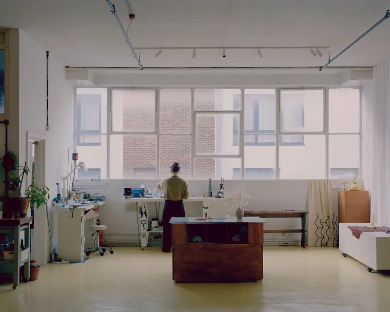 Interior workspace with person standing at desk beneath large industrial windows facing brick courtyard