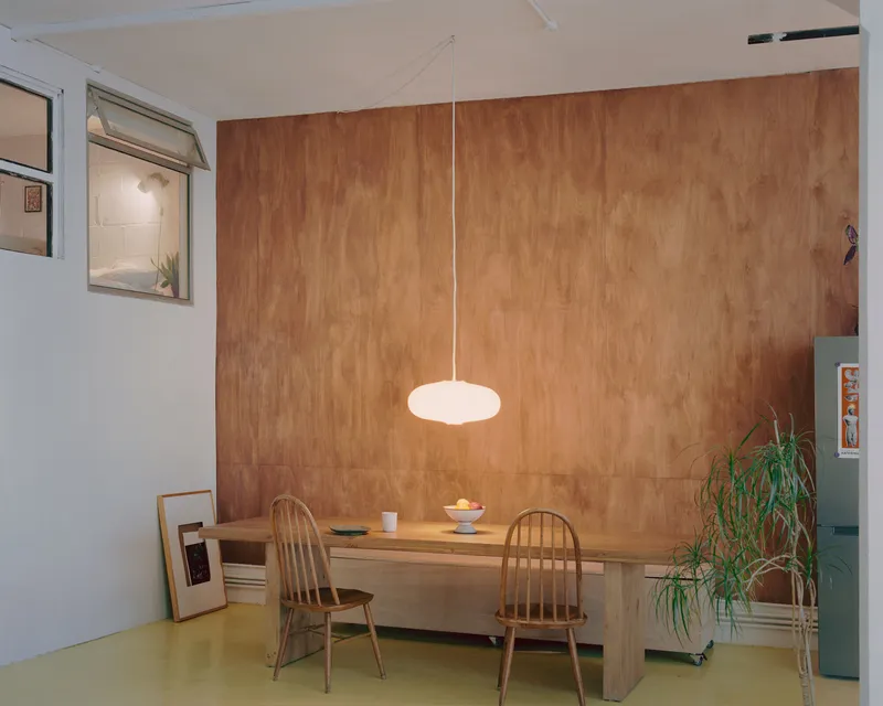 Dining space with plywood wall, suspended pendant light, and timber table on yellow flooring