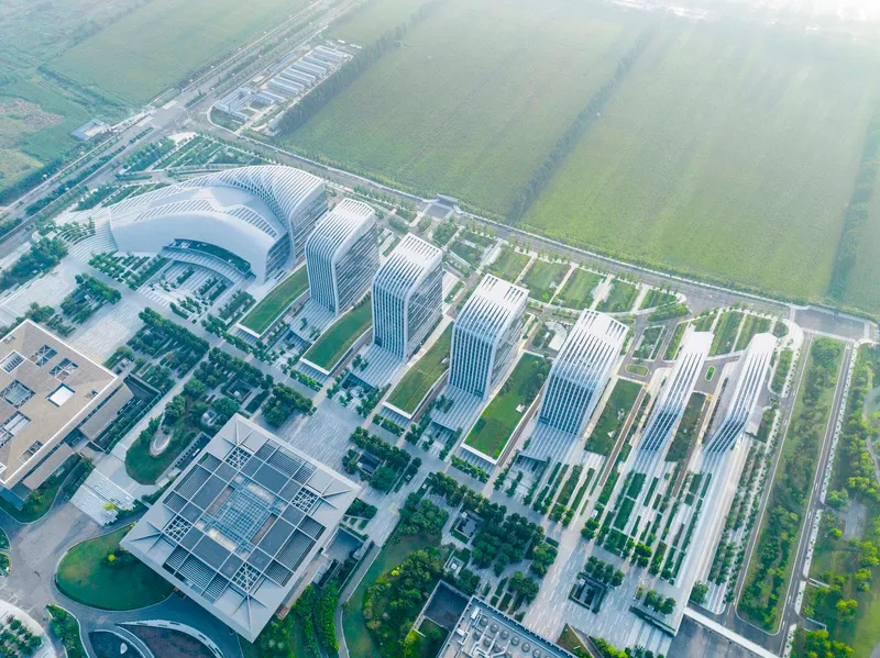 Drone view of horizontal louver facades on curved towers facing green agricultural fields in hazy light