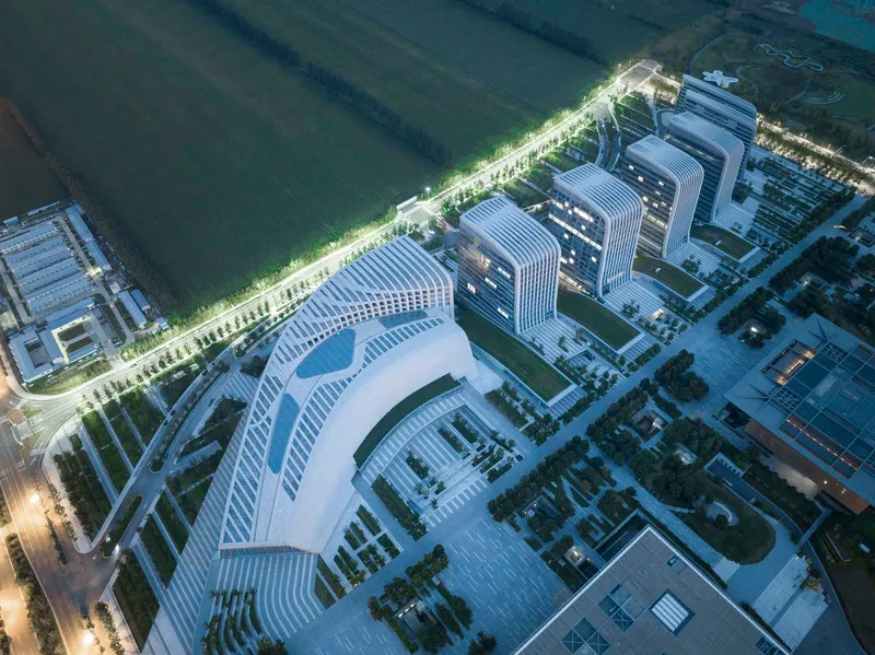 Nighttime aerial showing the illuminated curved tower and campus plaza adjacent to dark fields