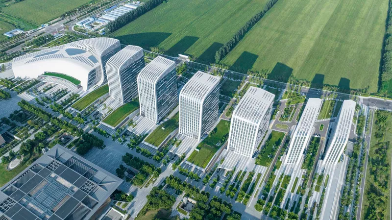 Aerial view of seven white-ribbed tower blocks arranged in two rows across landscaped grounds and green fields