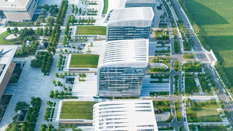 Drone view of three curved white-ribbed office buildings separated by green courtyards and paved plazas