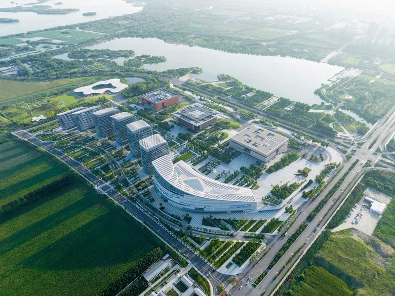 Aerial view of the campus showing curved building volumes and flat-roofed blocks beside green fields and waterways