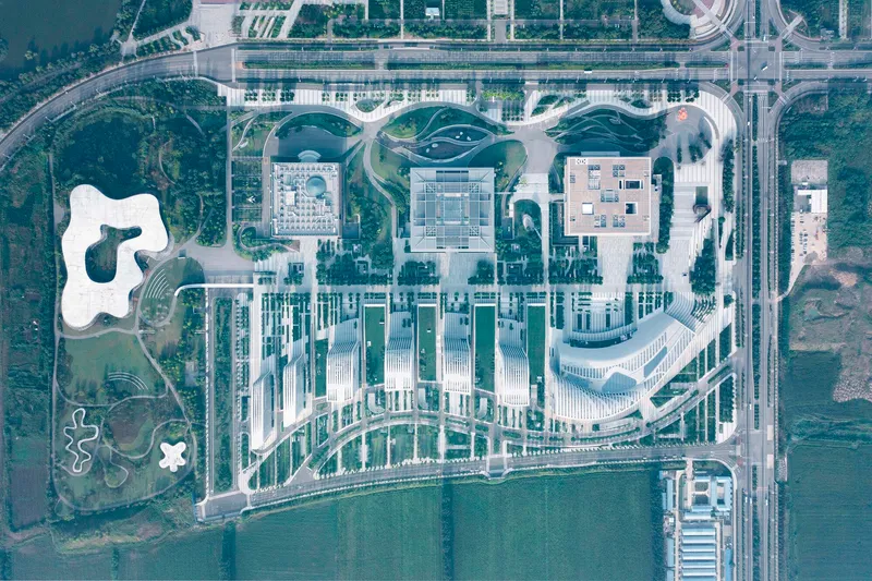 Aerial view of a campus with white ribbed towers and three organic-shaped roofs beside a waterfront