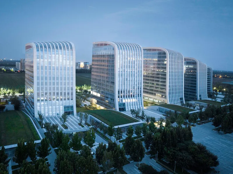 Row of illuminated white-ribbed glass towers at dusk surrounded by landscaped lawns and street trees
