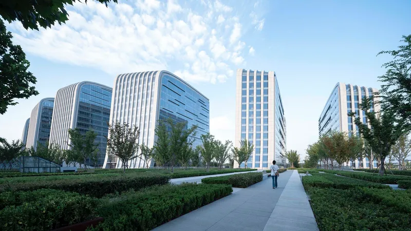 Pedestrian pathway through manicured hedges leading toward the towers under a blue sky with clouds