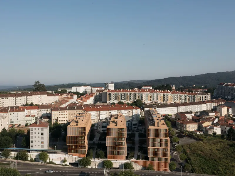 Elevated view of three timber-clad blocks among white apartment buildings at dusk