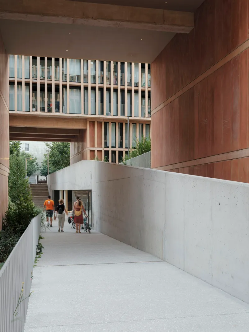 Sloped concrete passage with timber-clad soffit overhead and pedestrians approaching the walkway