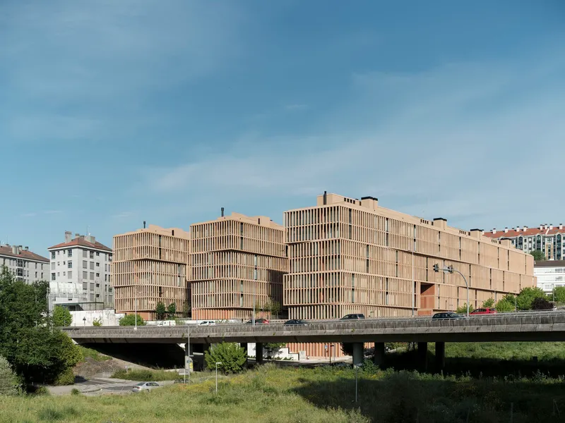 Long view of the timber-clad volume from across the concrete bridge and roadway