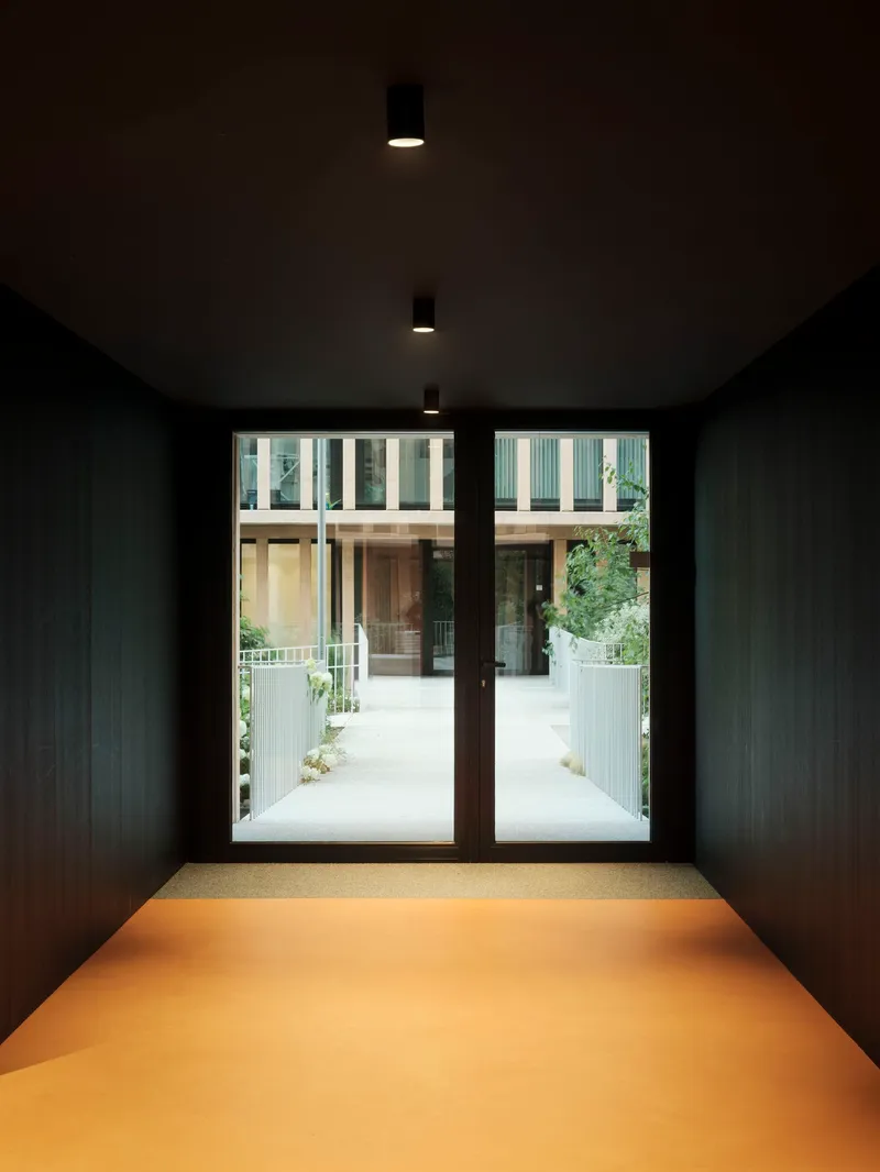 Dark vestibule with yellow resin floor and glass doors leading to the sunlit courtyard