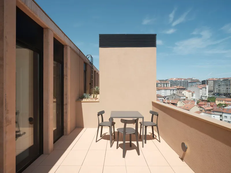 Rooftop terrace with dining furniture overlooking residential buildings under a clear blue sky