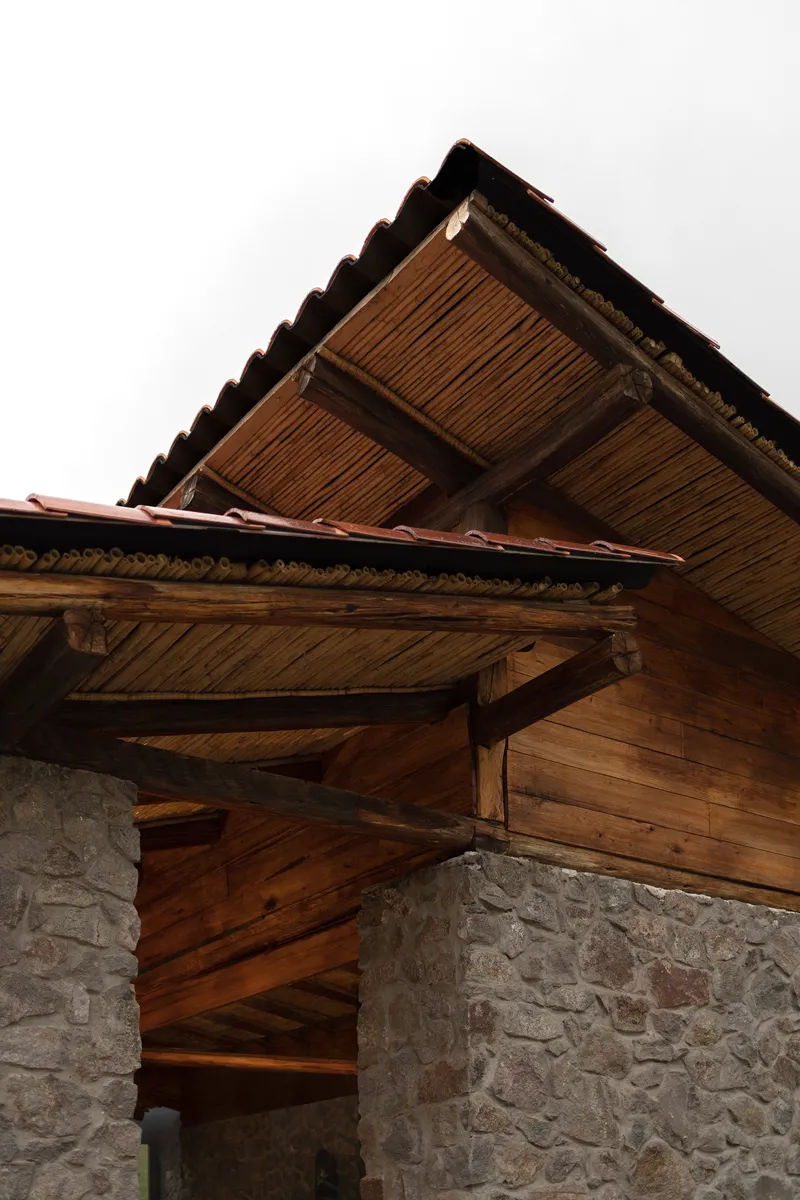 Upward view of the overhanging timber eaves and stone columns under overcast sky