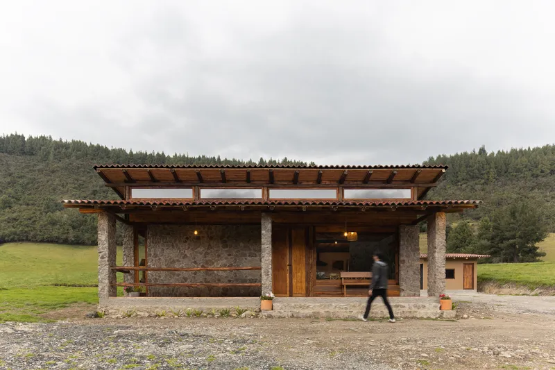 Stone pavilion with timber roof and clerestory windows as a figure walks past in an overcast rural landscape