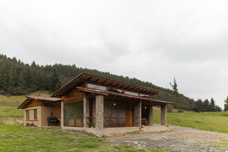 Exterior view of the stone and timber structure with wide eaves against forested hillside under grey skies