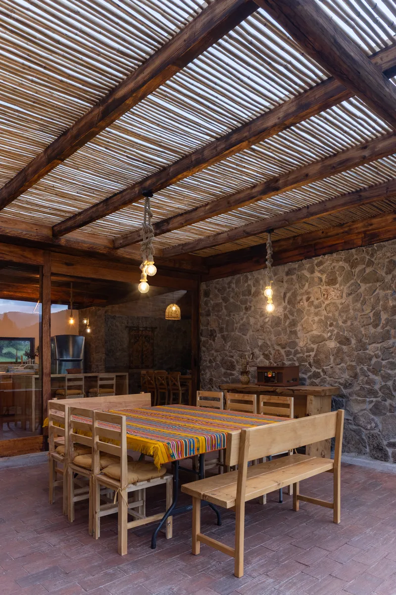 Covered dining area with timber beams, striped reed ceiling and fieldstone walls with pendant lighting