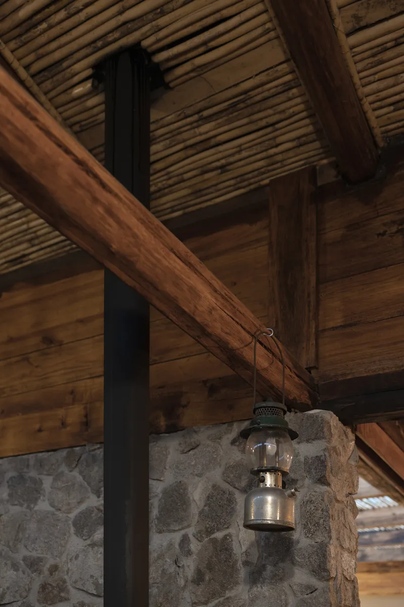 Detail of a vintage lantern hanging from timber beams above a stone and metal column junction