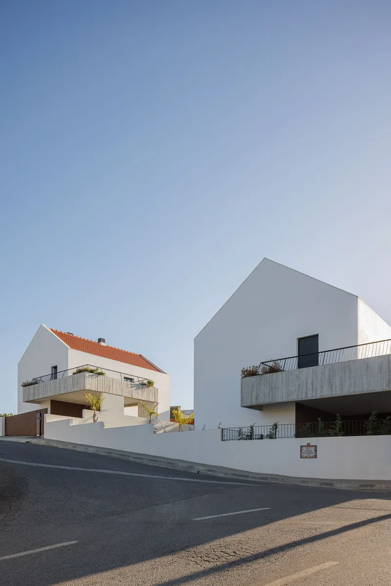 Corner view showing two white gabled volumes with concrete balconies and orange clay tile roofs from the street